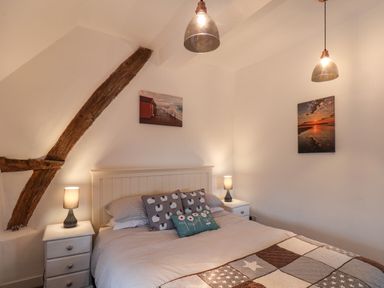A bedroom with a double bed two bedside tables with lamps wooden ceiling beams and two pictures on the walls at Lythe Cottage in Lythe