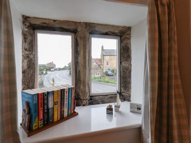A window with stone frame and books on the windowsill with small decorative items at Lythe Cottage in Lythe