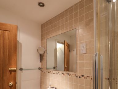 A bathroom wall with a mirror shelves and a tiled section with a shower cabin at Lythe Cottage in Lythe