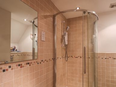 A bathroom with a glass shower enclosure a hand shower mounted on tiled walls and a mirror reflecting part of the opposite wall at Lythe Cottage in Lythe