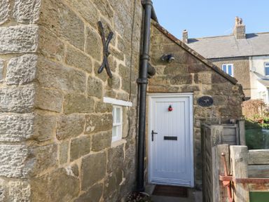 The stone exterior of a cottage with a white wooden door and small window at Lythe Cottage in Lythe