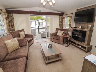 A living room with brown sofas glass coffee table wall mounted tv and sliding glass doors at Lakeside Haven in Carnforth