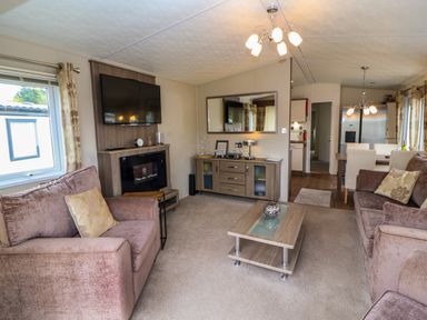A living room with sofas a coffee table a wall mounted tv and a dining area at Lakeside Haven in Carnforth