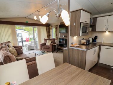 An open-plan living room and kitchen with sofa armchair dining table and kitchen appliances at Lakeside Haven in Carnforth