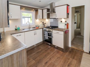 A kitchen with cabinets stove and sink with window above at Lakeside Haven in Carnforth