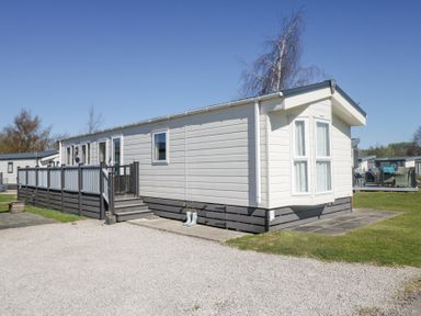 A white mobile home with a deck and steps in a park setting at Lakeside Haven in Carnforth