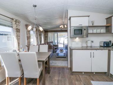 A dining table with four chairs next to a kitchen area with a microwave kettle and toaster at Lakeside Haven in Carnforth