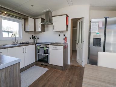 A kitchen with white cabinets stove and refrigerator next to a door at Lakeside Haven in Carnforth