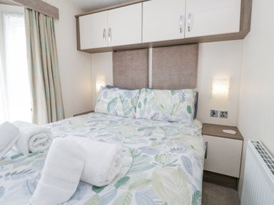 A bedroom with a bed with leaf patterned bedding and rolled white towels at Lakeside Haven in Carnforth