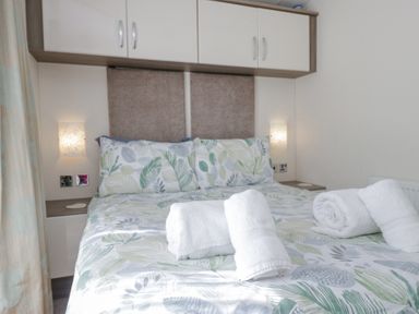 A bedroom with a bed with leaf patterned bedding and rolled white towels at Lakeside Haven in Carnforth