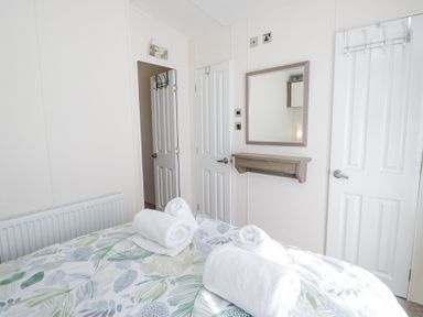 A bedroom with a bed and rolled towels on it two doors a mirror and a radiator at Lakeside Haven in Carnforth