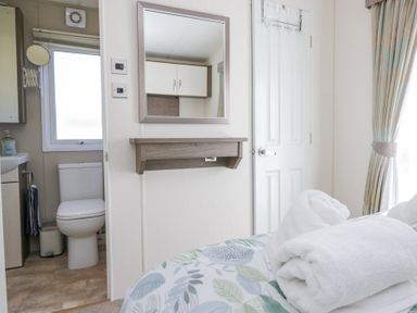 A bedroom with folded towels on bed a door with hooks and a bathroom with a toilet at Lakeside Haven in Carnforth