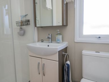 A bathroom sink with soap dispenser next to a toilet and a shower area at Lakeside Haven in Carnforth