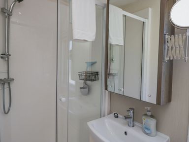 A bathroom with a shower area towel hanging on glass door a sink with liquid soap and a mirrored cabinet at Lakeside Haven in Carnforth