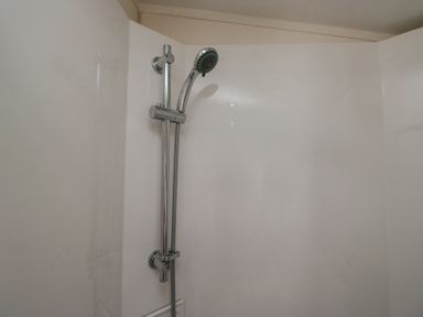 A shower area with a chrome adjustable showerhead on a white wall at Lakeside Haven in Carnforth