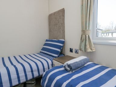 A small bedroom with two single beds with blue and white striped bedding and a window at Lakeside Haven in Carnforth
