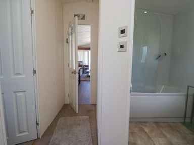 A hallway with a door opening to a living room and a bathroom with a bathtub at Lakeside Haven in Carnforth