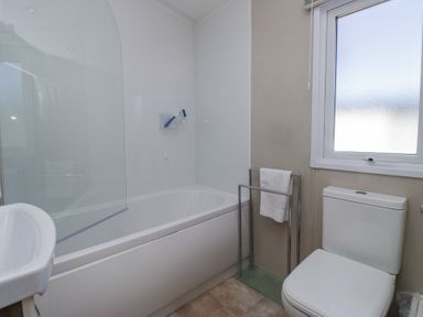 A bathroom with a bathtub a toilet a towel rack and a window at Lakeside Haven in Carnforth