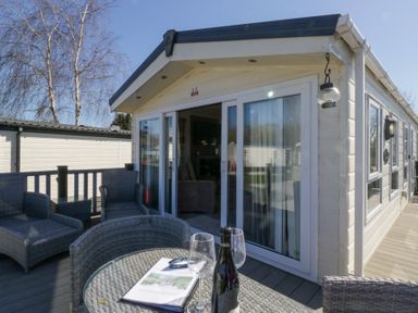 An outdoor patio area with wicker furniture and a table with wine glasses and a bottle at Lakeside Haven in Carnforth