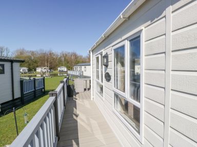 A deck area with railing and outdoor furniture next to a row of mobile homes at Lakeside Haven in Carnforth