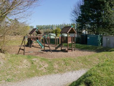 An outdoor playground with slides swings and climbing structures surrounded by grass and trees at Lakeside Haven in Carnforth