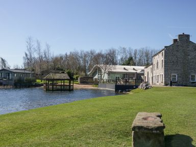 A lakeside view with a stone building deck and gazebo over water at Lakeside Haven in Carnforth