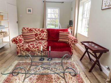 A living room with a patterned sofa glass coffee table and a wooden side table at Kyleatunna Cottage in Ennis County Clare