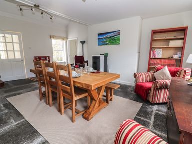 A dining room with a wooden table and six chairs a red striped armchair a red bookshelf and a painting on the wall at Kyleatunna Cottage in Ennis County Clare