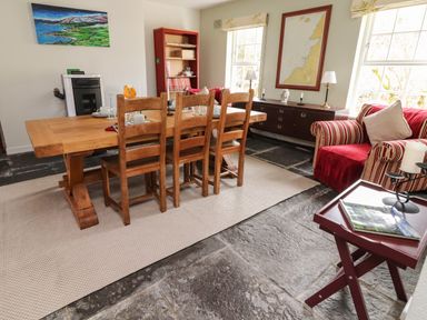 A dining room with a wooden table and chairs a striped armchair and windows at Kyleatunna Cottage in Ennis County Clare
