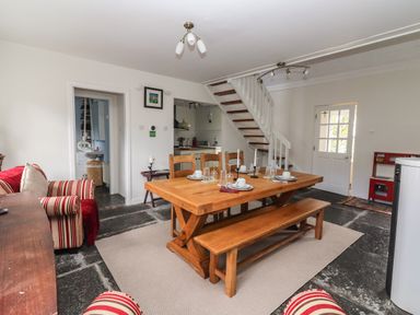 A dining area with a wooden table and chairs near a staircase and door at Kyleatunna Cottage Ennis County Clare