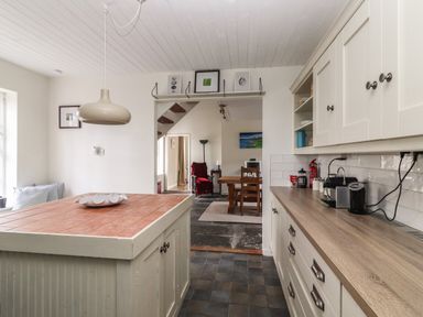 A kitchen with a tiled island and wooden countertop leading into a dining room with a wooden table and chairs at Kyleatunna Cottage in Ennis County Clare