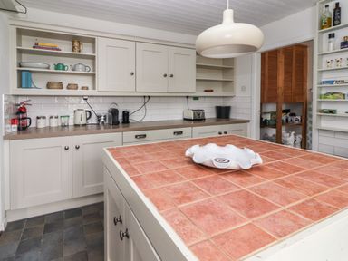 A kitchen with white cabinets a tiled island countertop appliances and open shelving at Kyleatunna Cottage in Ennis County Clare