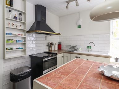A kitchen with a black stove and hood white tiled walls a sink and a red tiled countertop at Kyleatunna Cottage in Ennis County Clare