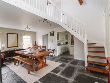 A dining area with wooden table and bench next to staircase and kitchen at Kyleatunna Cottage in Ennis County Clare