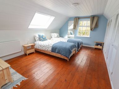 A bedroom with two single beds a skylight window a blue accent wall and wooden floor at Kyleatunna Cottage in Ennis County Clare