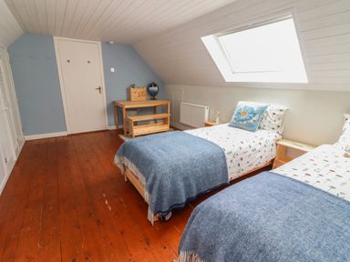 A bedroom with two single beds blue blankets and floral bedding a wooden floor a desk with a mirror and a skylight window at Kyleatunna Cottage in Ennis County Clare