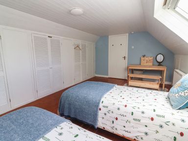 A bedroom with two single beds, built-in white wardrobes, a wooden table and bench under a slanted ceiling at Kyleatunna Cottage in Ennis County Clare