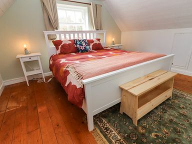 A bedroom with a white bed frame red floral bedding two nightstands with lamps wooden floor and a green patterned rug at Kyleatunna Cottage in Ennis County Clare