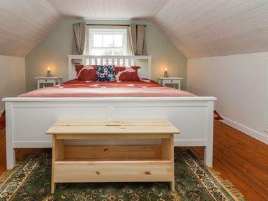 A bedroom with a white bed frame red bedspread and wooden bench at Kyleatunna Cottage in Ennis County Clare