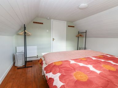A bedroom with a bed covered in a floral blanket and two clothes racks with hangers at Kyleatunna Cottage in Ennis County Clare