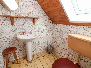 A bathroom with a floral wallpaper wooden stool pedestal sink shelf with jars and a toilet under a skylight at Kyleatunna Cottage in Ennis County Clare