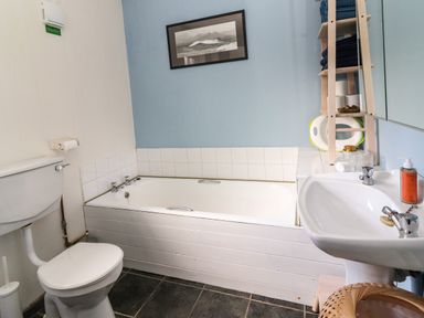 A bathroom with a bathtub toilet and sink with shelving holding towels and toilet paper at Kyleatunna Cottage in Ennis County Clare