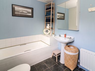 A bathroom with a bathtub sink mirror wooden shelf and wicker laundry basket at Kyleatunna Cottage in Ennis County Clare