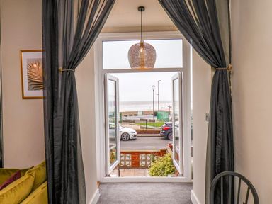 A room with black curtains framing an open window showing a view of parked cars and the beach at Apt 3 @ Hunter's Quay in Bridlington