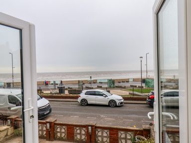 View through open doors showing a street with parked cars and a sea wall with people walking by the ocean at Apt 3 @ Hunter's Quay in Bridlington