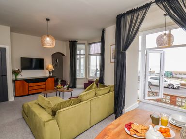 A living room with a green sofa facing a TV mounted on the wall at Apt 3 @ Hunter's Quay in Bridlington