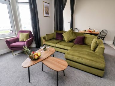 A living room with a green sectional sofa purple armchair wooden coffee tables and a dining table at Apt 3 @ Hunter's Quay Bridlington