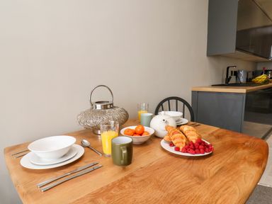 A wooden dining table set with plates bowls cutlery glasses of orange juice croissants raspberries and a teapot in a kitchen at Apt 3 @ Hunters Quay in Bridlington