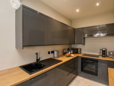 A kitchen with gray cabinets wooden countertops a black sink a kettle a microwave a coffee machine and a toaster at Apt 3  Hunter's Quay in Bridlington