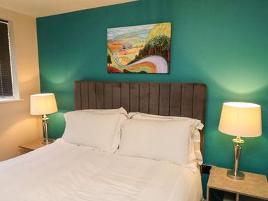 A bedroom with a bed with white linens and pillows two bedside tables with lamps and a painting above the bed at Apt 3 @ Hunter's Quay in Bridlington